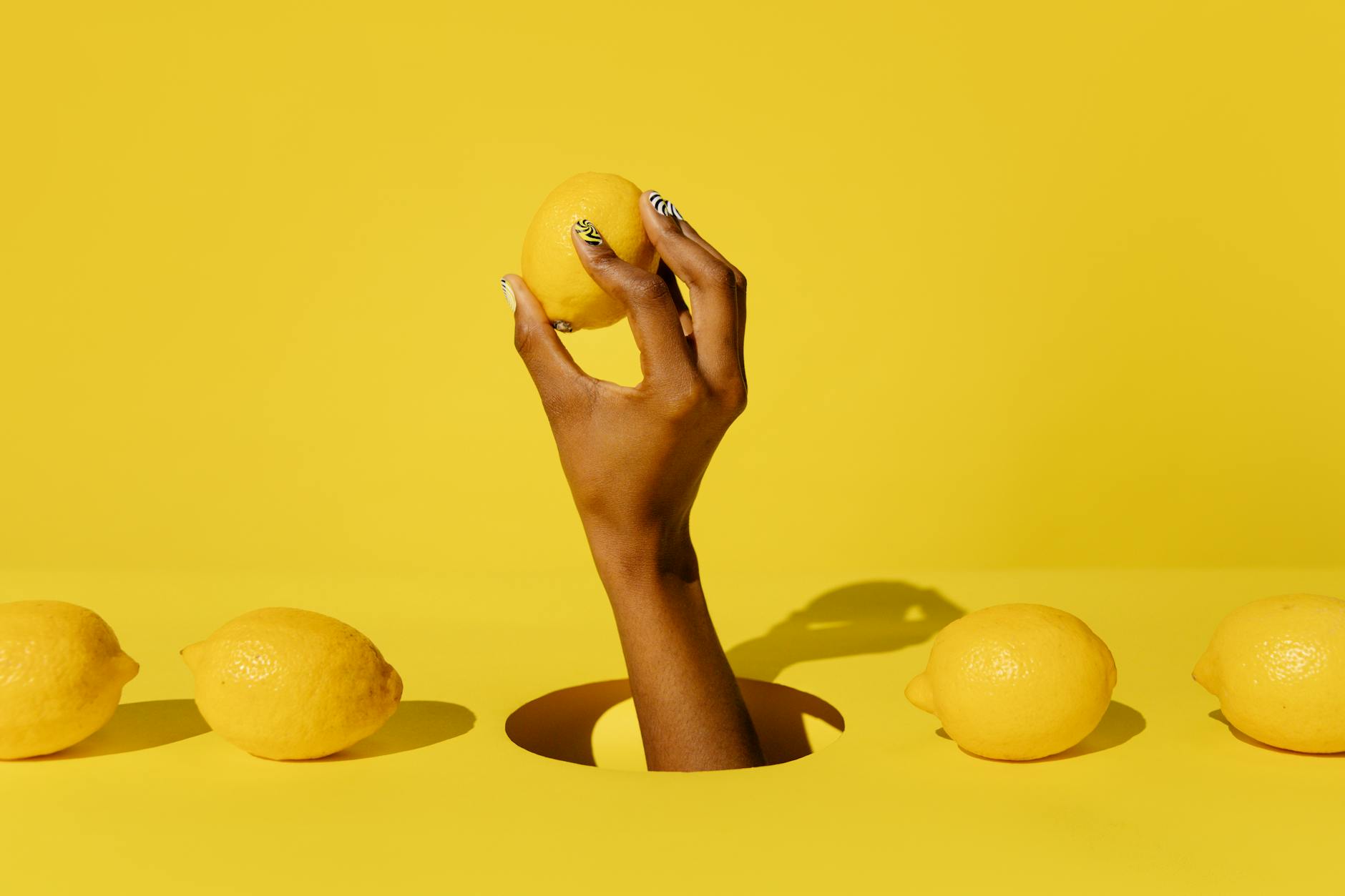 A hand holding a fresh lemon against a vivid yellow background, symbolizing sensitivity and vibrancy