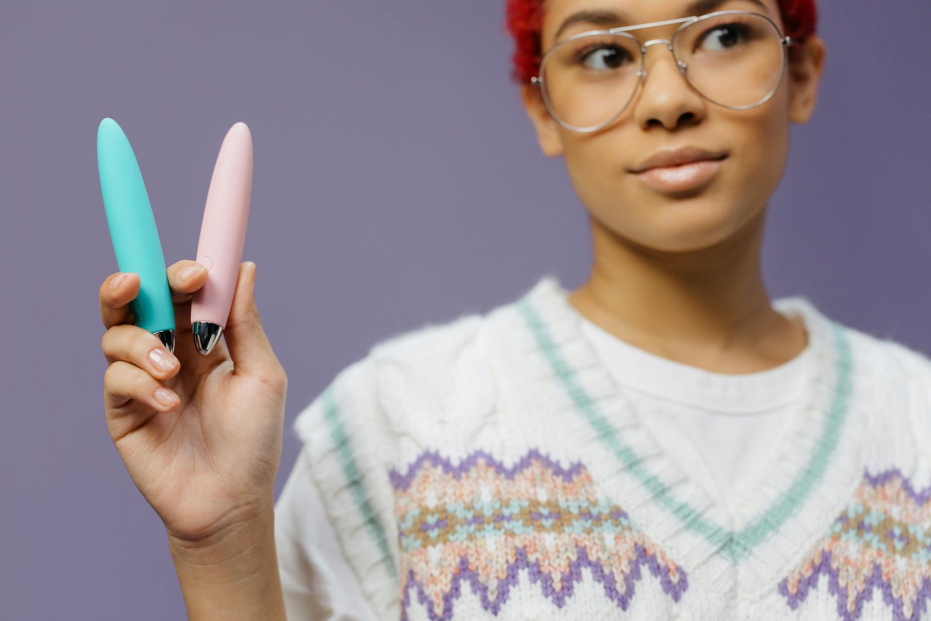Two hands holding pastel-colored silicone vibrators against a soft background