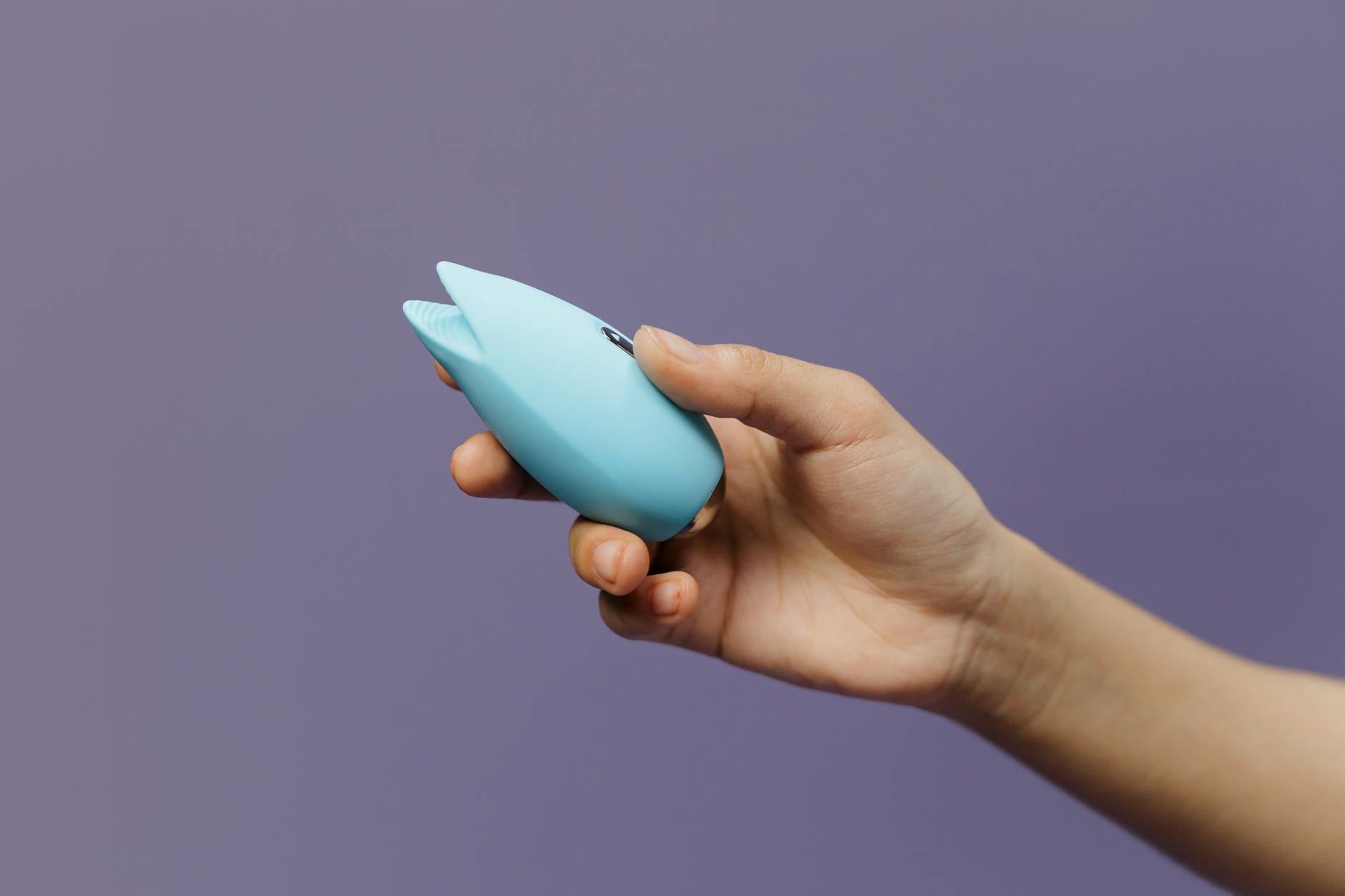 A yellow lemon vibrator held in hand against a purple background, representing clitoral sensation and self-care.