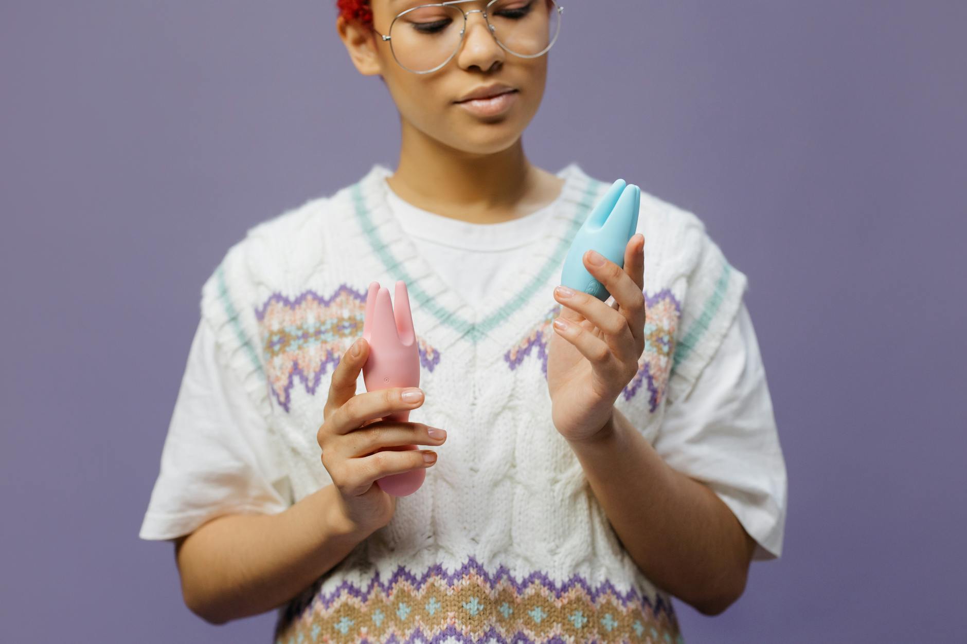 Woman thoughtfully holding colorful silicone vibrators, considering which one to use for pleasure