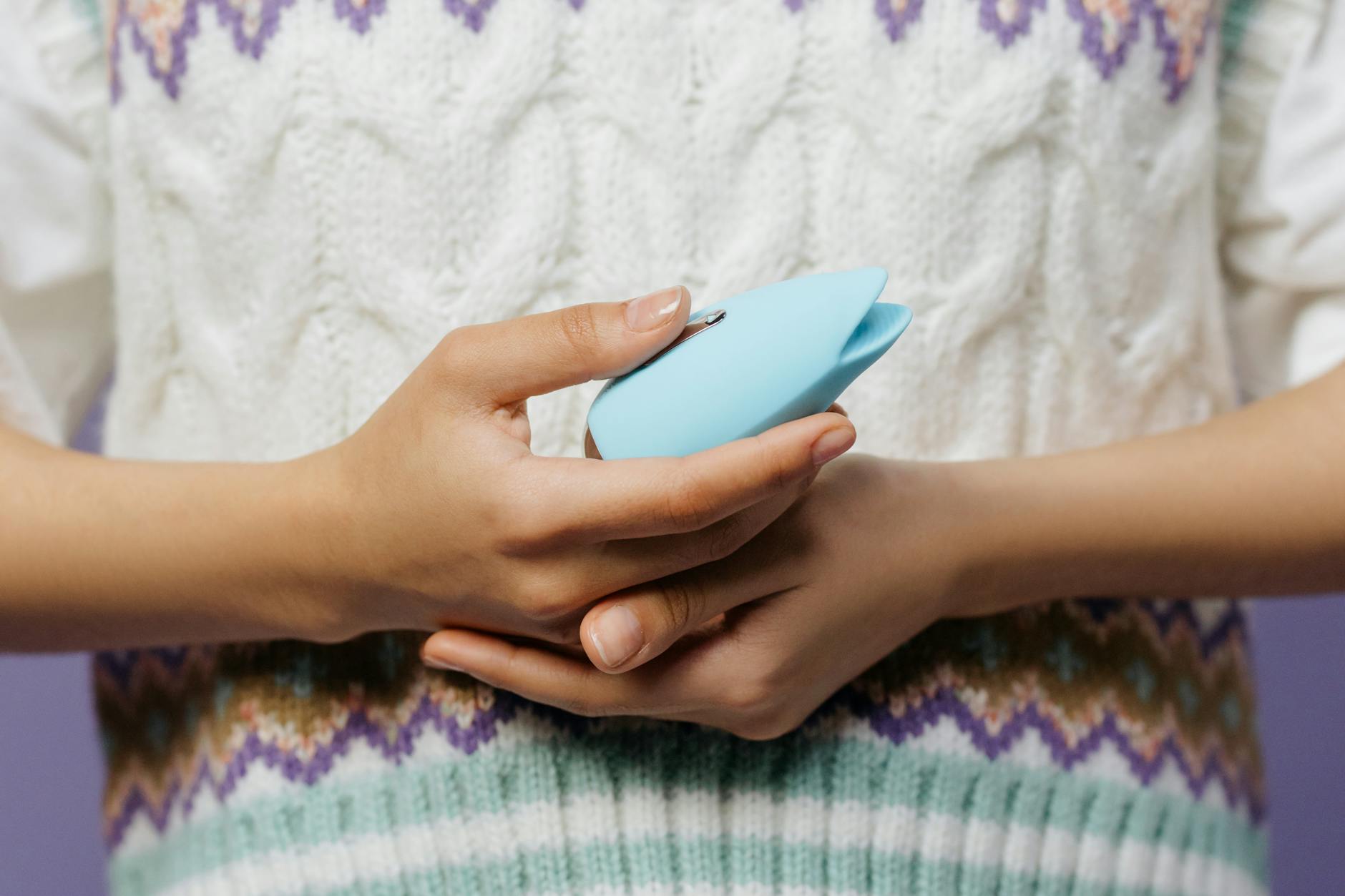 Close-up of a hand holding a blue personal massager against a knitted sweater